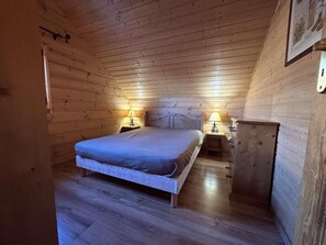 Un dormitorio de cabaña de madera con una cama, dos mesitas de noche y un aparador.