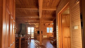 Interior amplio de una cabaña de madera con comedor, cocina y una escalera que conduce a un nivel superior.