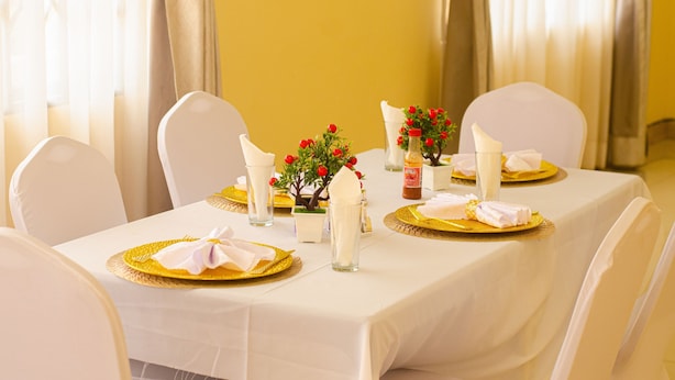 Une table à manger agrémentée de chaises blanches, de sets de table dorés et de fleurs rouges.