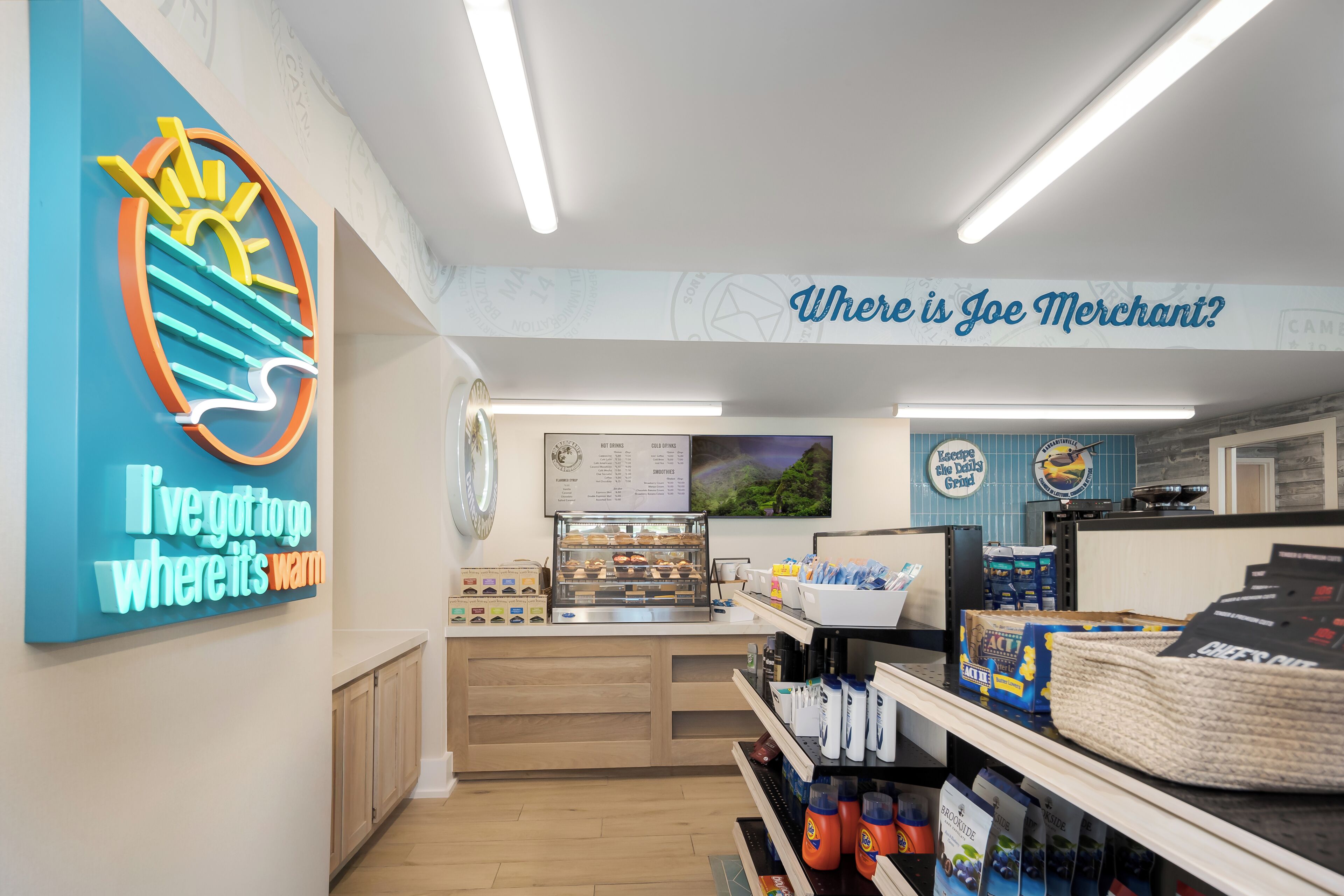 A cafe with a neon sign, a menu board, and a counter with baked goods.