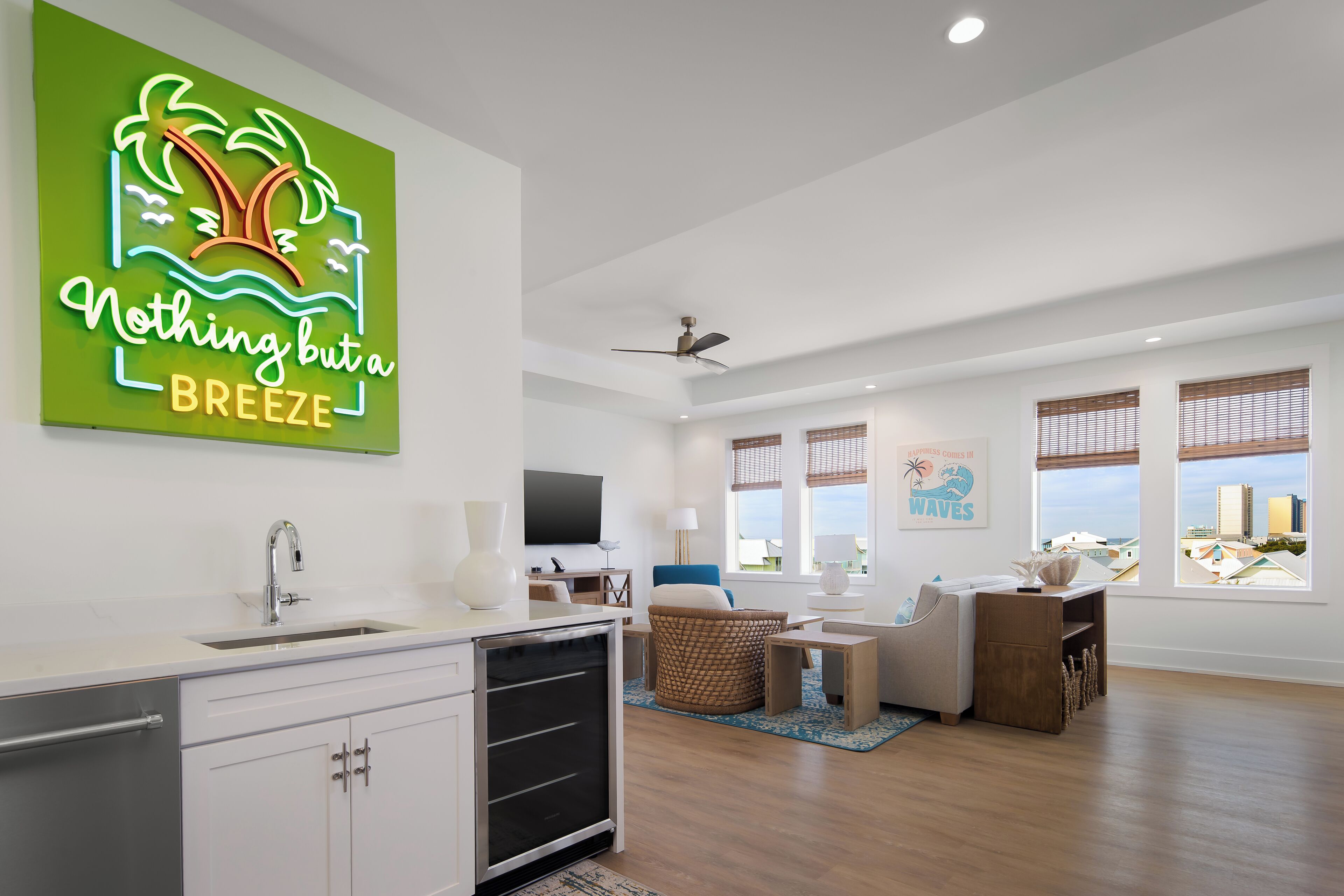 A modern living room with a kitchen area, large windows, and a ceiling fan.