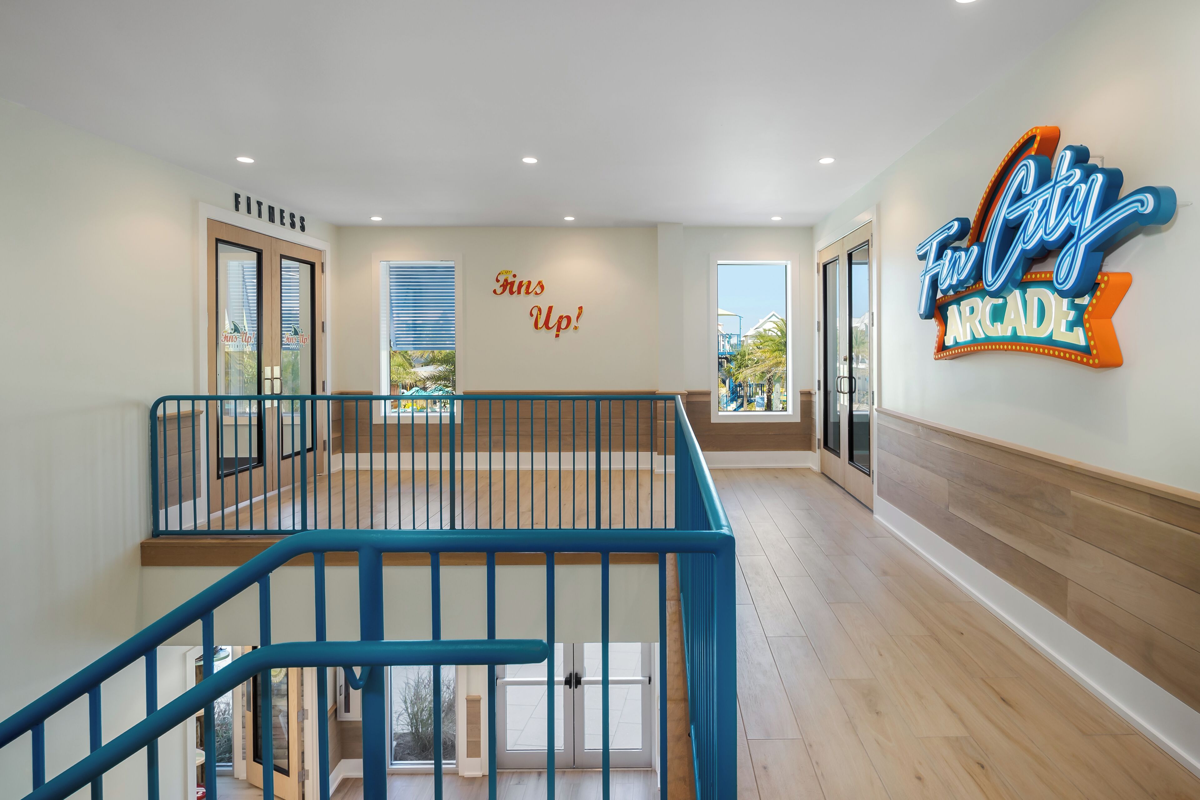 A spacious indoor area with a blue railing, a sign reading 'Fins Up!', and a neon sign for 'Fun City Arcade'.