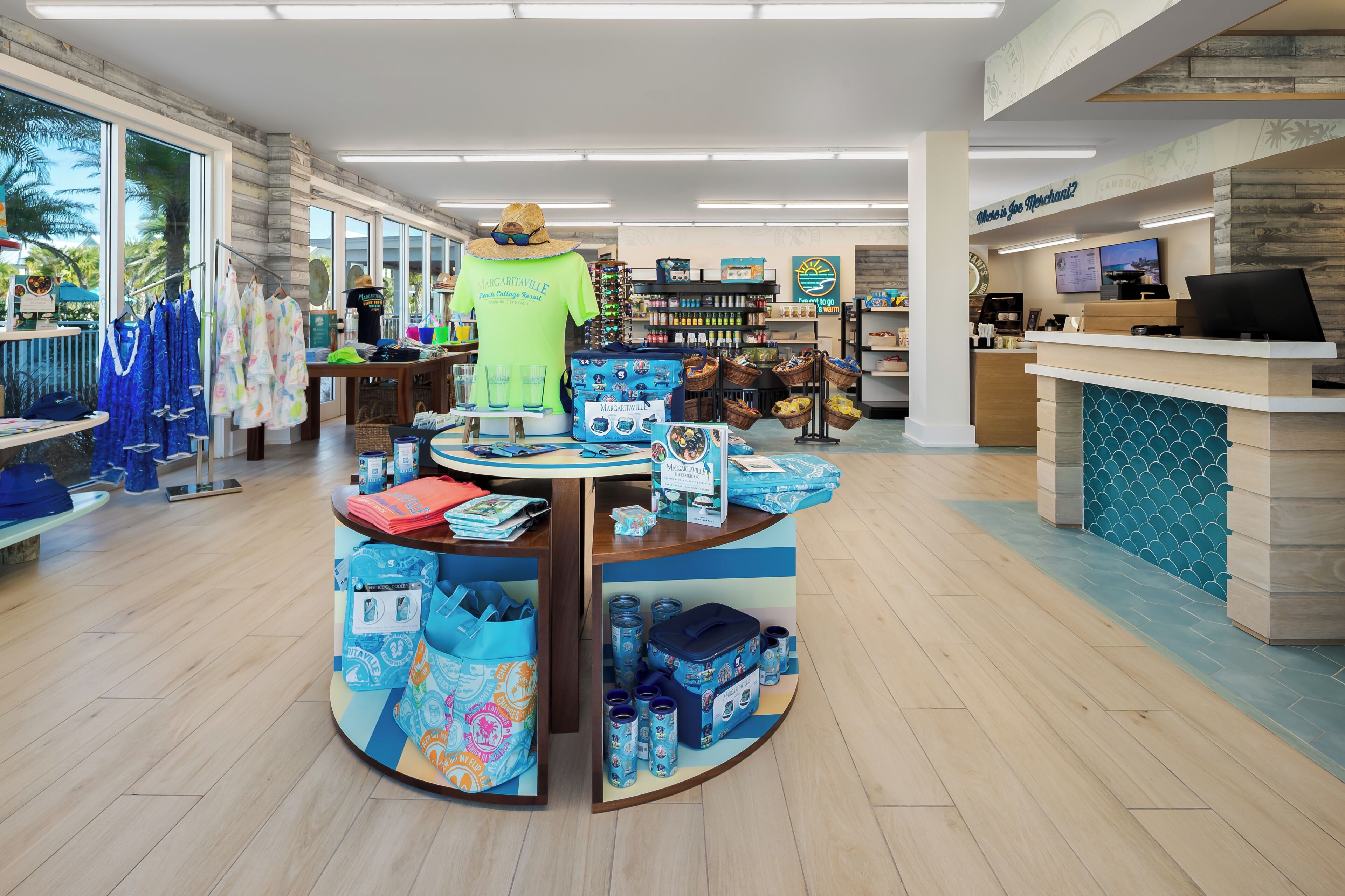 A retail store with a checkout counter, display tables with merchandise, and a large window with a view of palm trees.