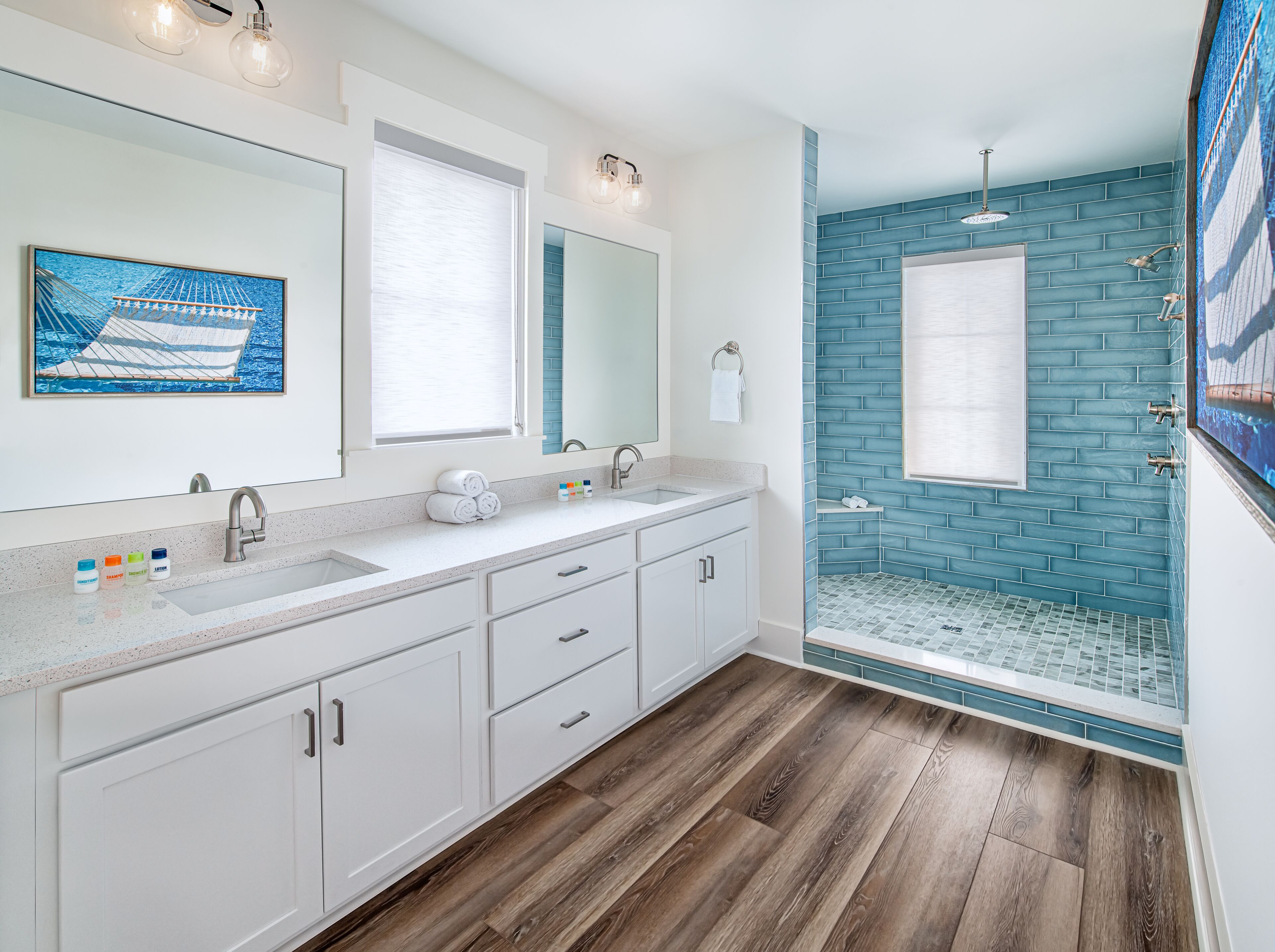 Une salle de bain moderne avec un grand miroir, deux lavabos, une douche aux carreaux bleus et un revêtement de sol en bois.