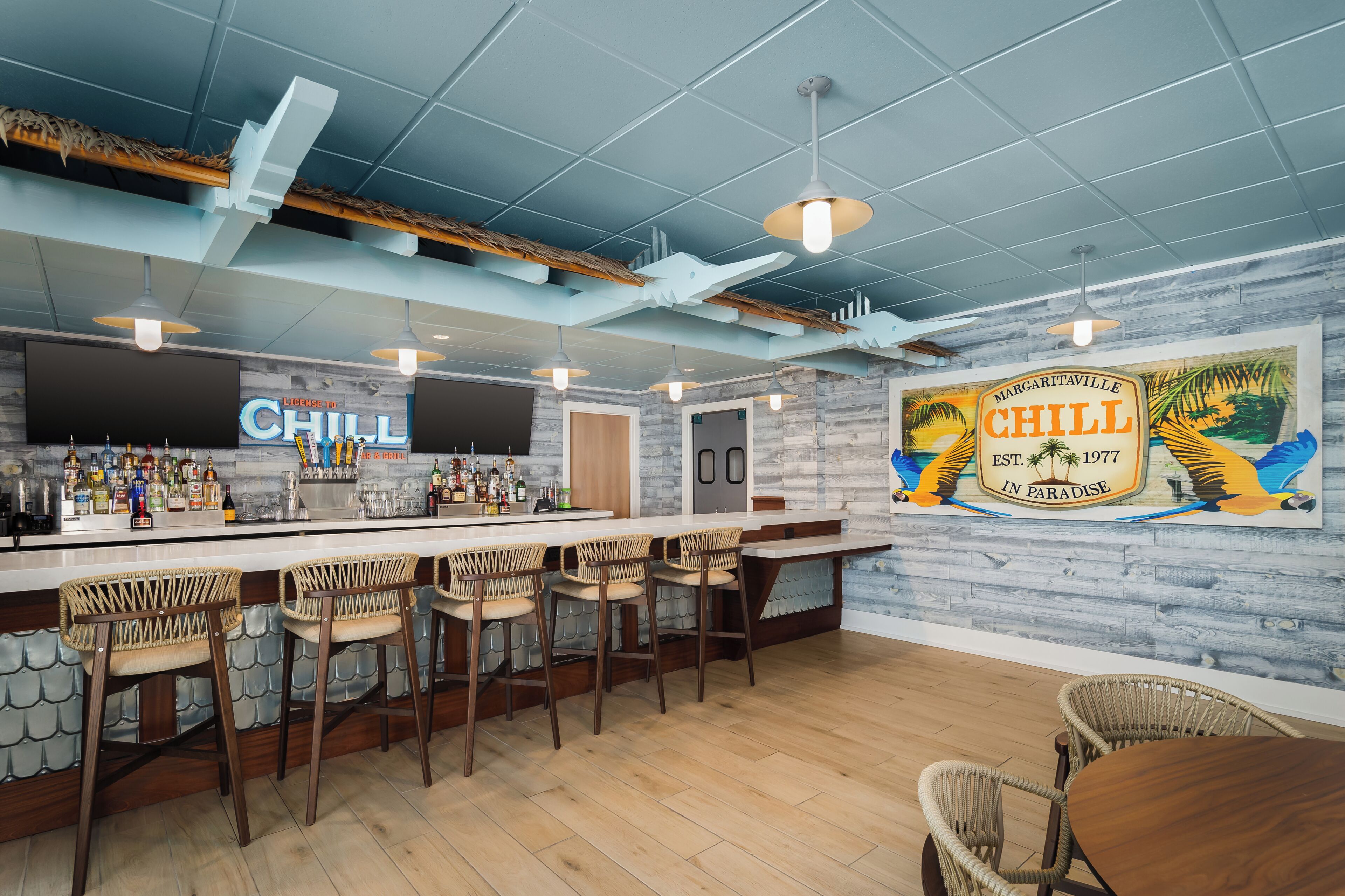 A bar area with a long counter, wicker chairs, and a mural of a beach scene.