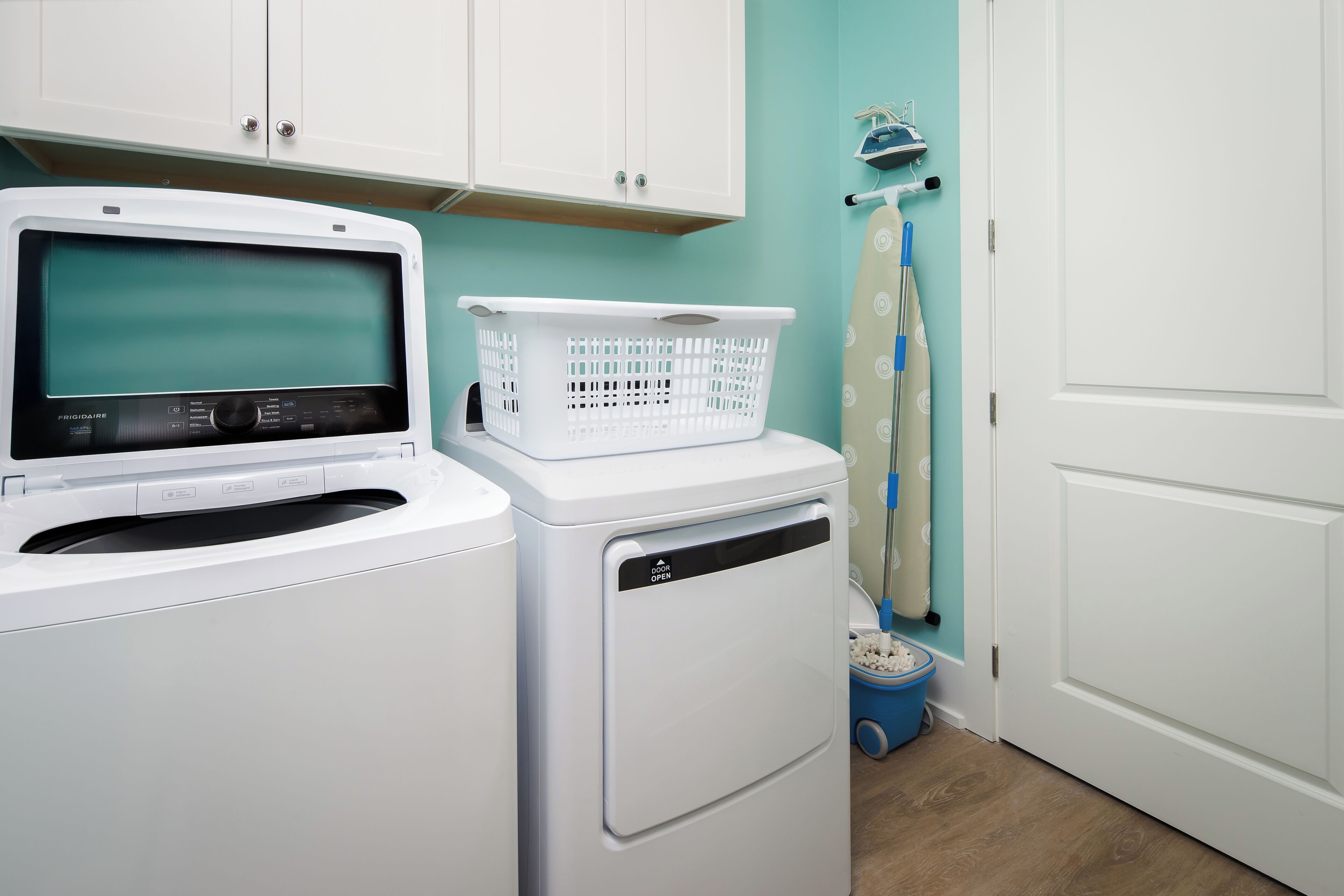 A laundry room with a front-loading washer and dryer, a white basket on the dryer, and a blue laundry basket on the floor.
