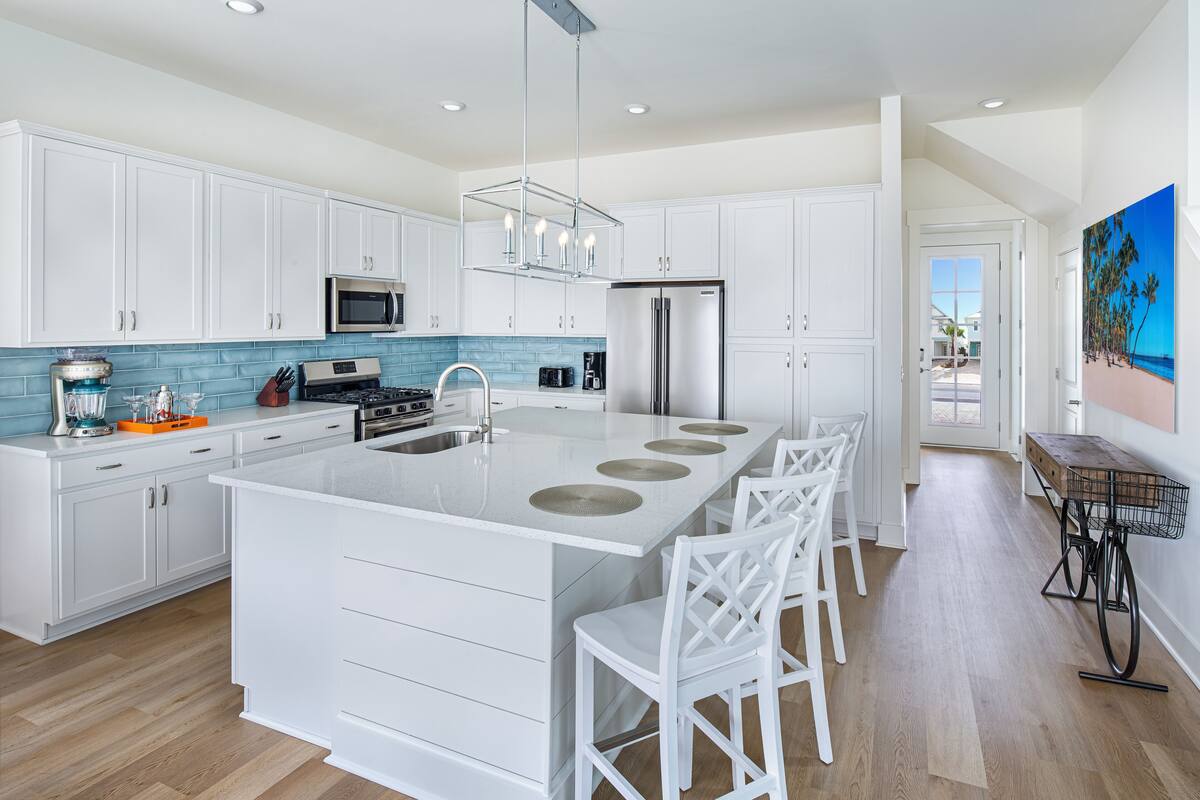 Una cocina moderna con armarios blancos, una isla central con taburetes y un refrigerador de acero inoxidable, además de un salpicadero con azulejos azules.