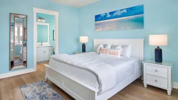 A bedroom with a bed, nightstands, a mirror, and a painting of a beach scene.