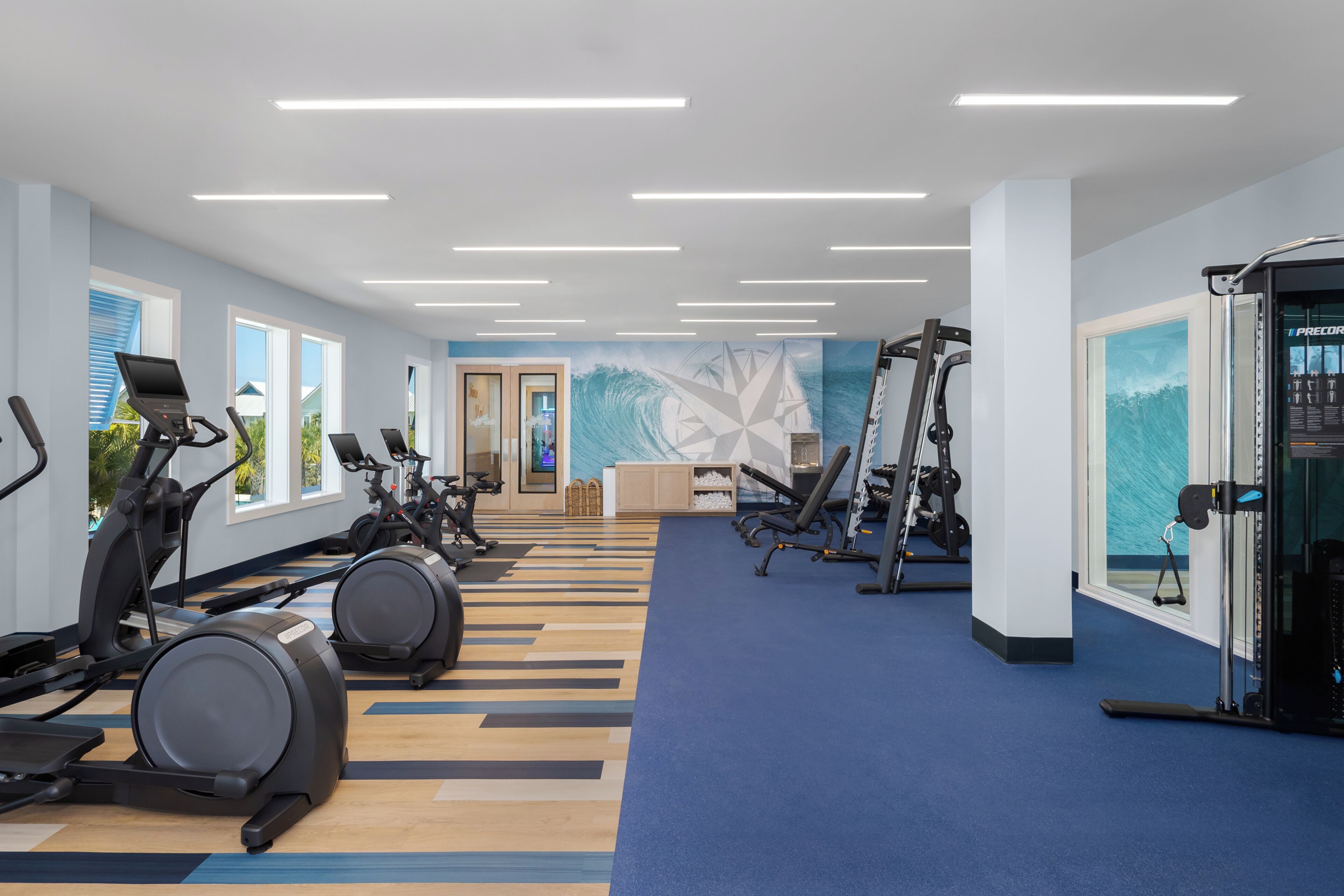 Een sportschool met trainingsapparatuur, een blauw tapijt en een groot raam.