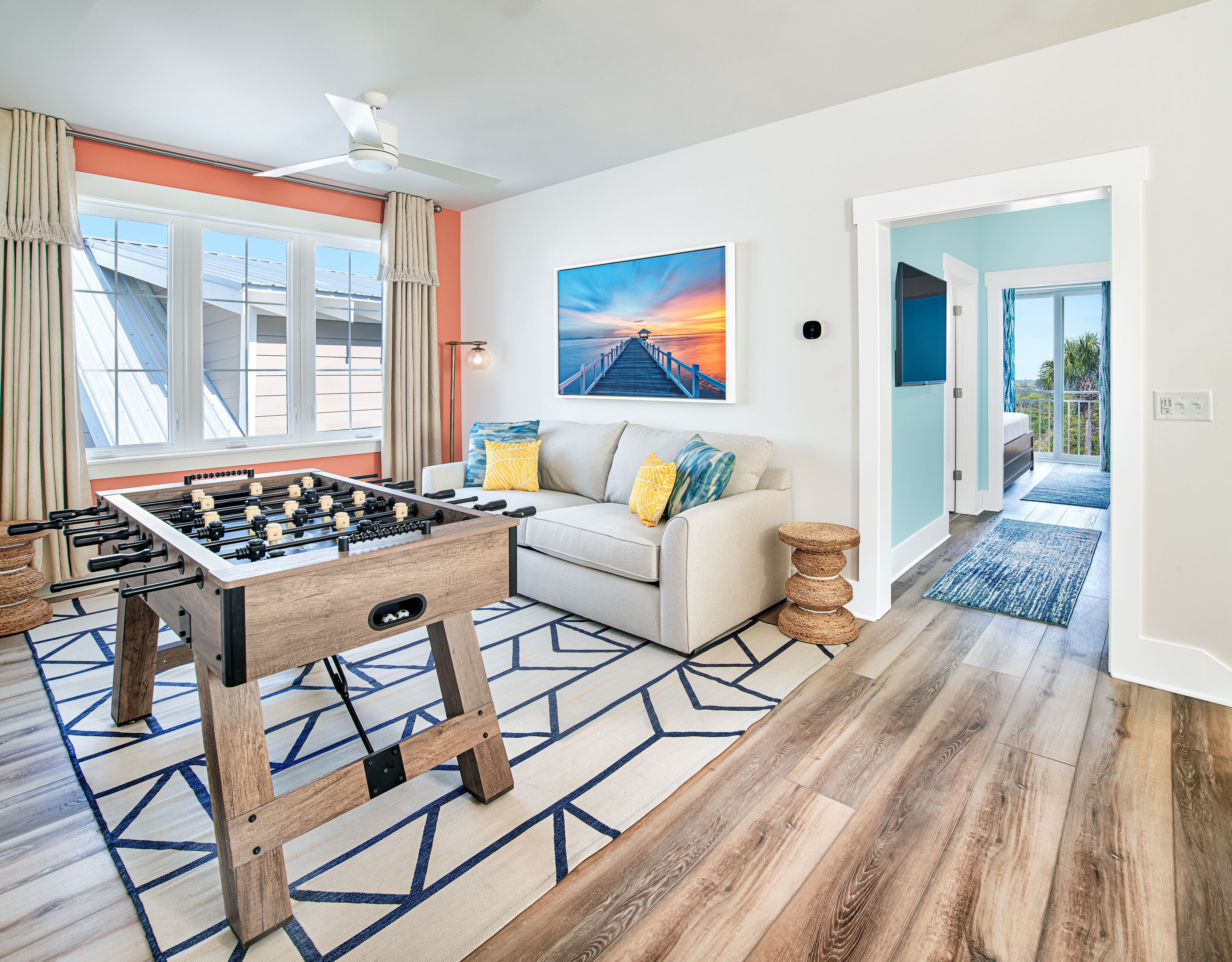 A room with a foosball table, a sofa with colorful cushions, and a painting of a sunset.