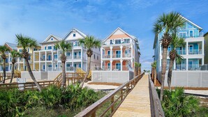 A wooden boardwalk leading to a beachfront hotel with multiple balconies and palm trees. - Margaritaville Beach Cottage Resort PCB (Panama City Beach)