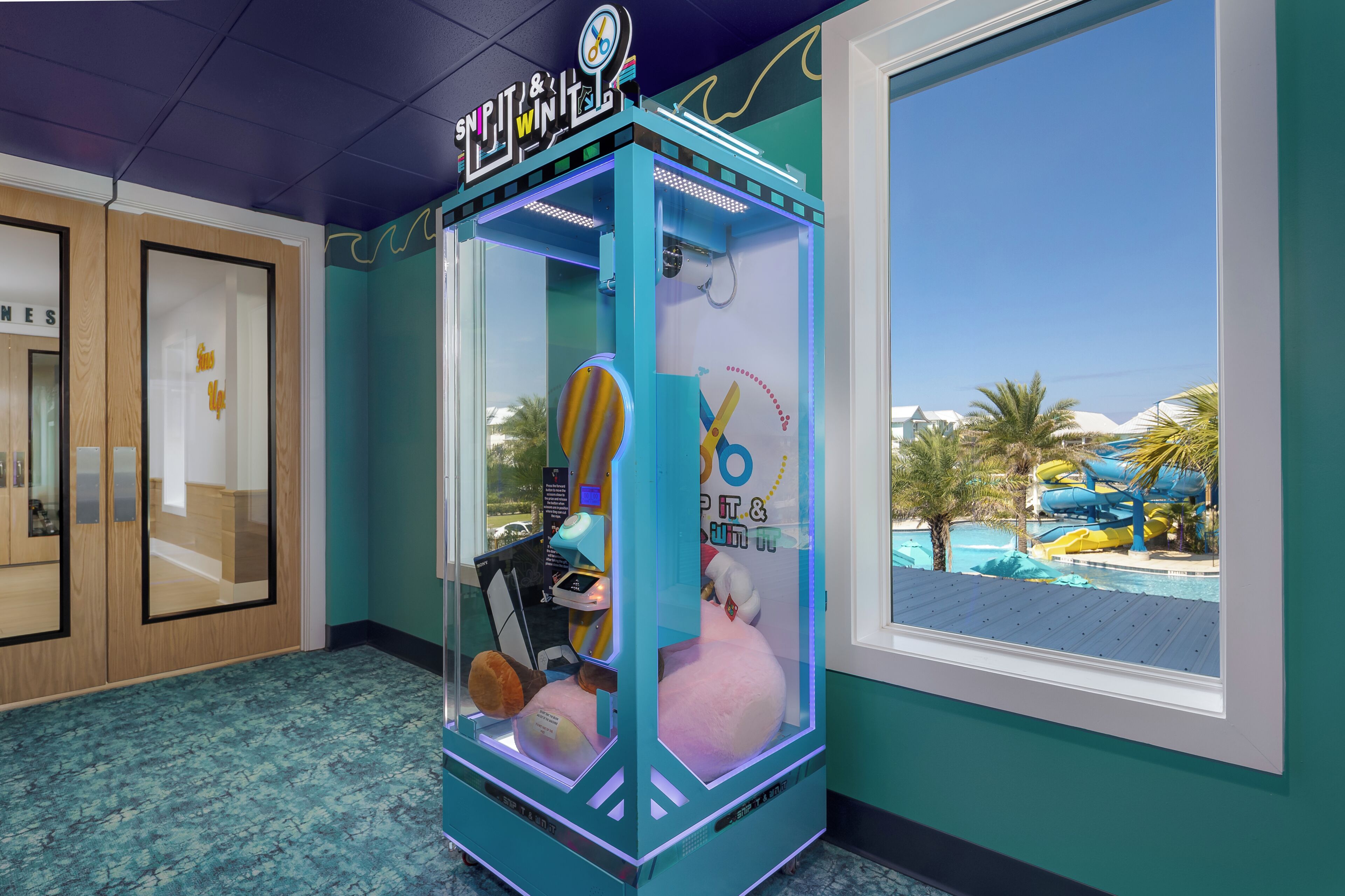A claw machine with plush toys inside, located in a room with a view of a water park.