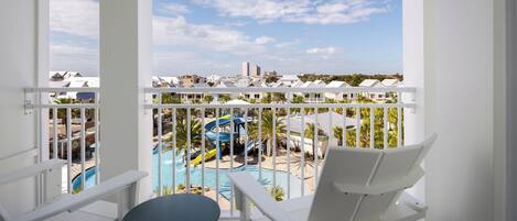 Un balcón con sillas y una mesa blancos, con vistas a una zona de piscina que incluye un tobogán y sillas de descanso.