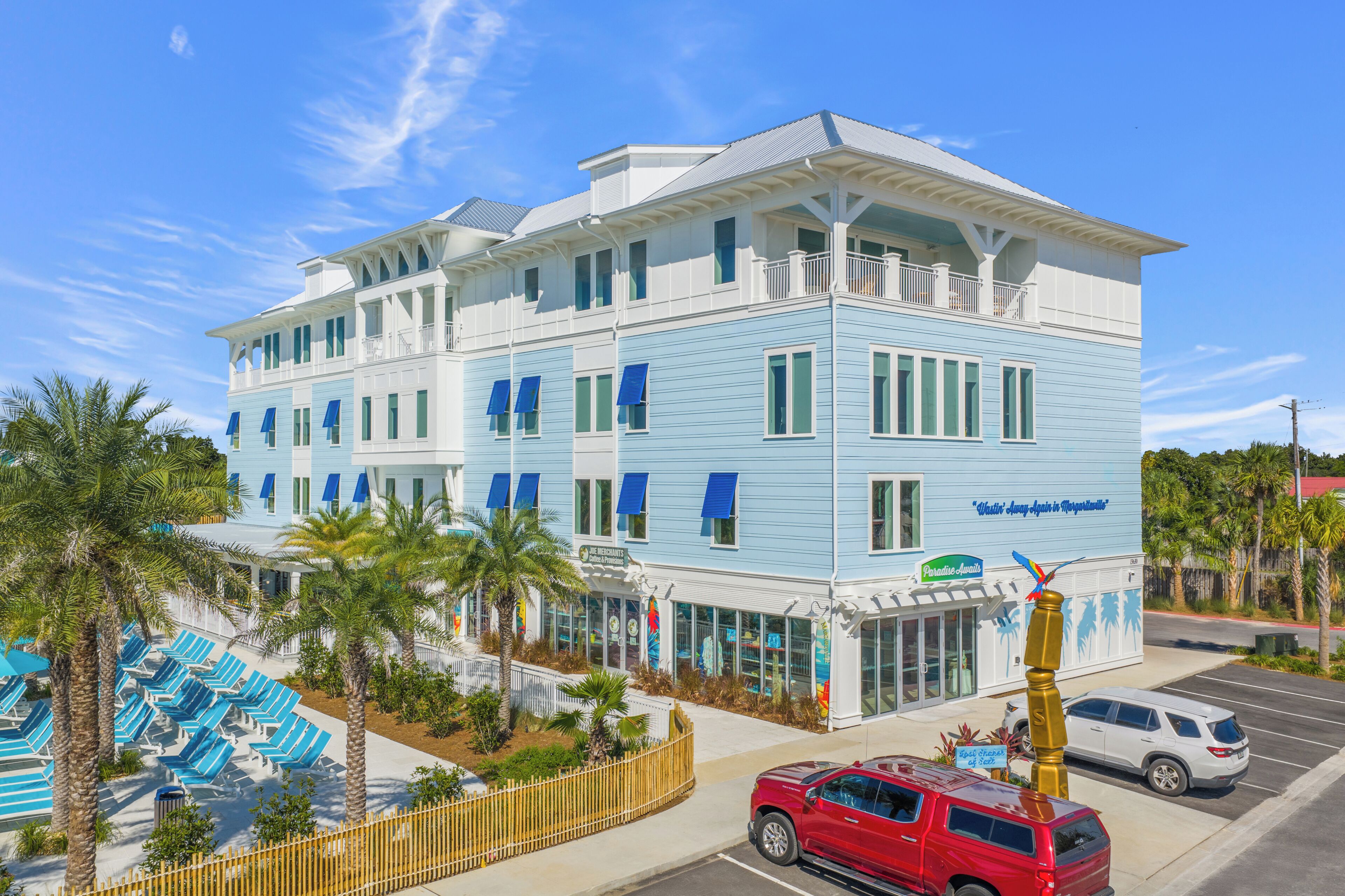 A hotel with a light blue exterior, multiple balconies, and a pool area with blue lounge chairs.