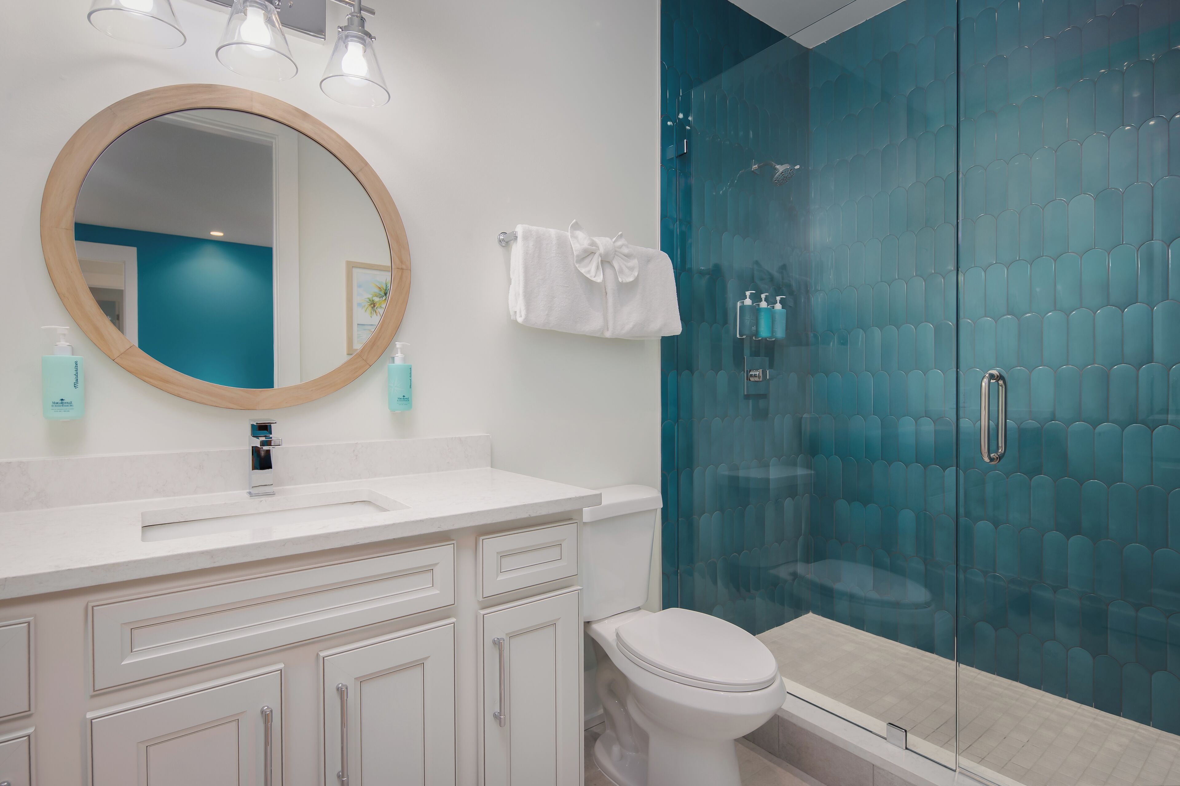 A bathroom with a round mirror, white cabinets, a toilet, and a glass-enclosed shower.