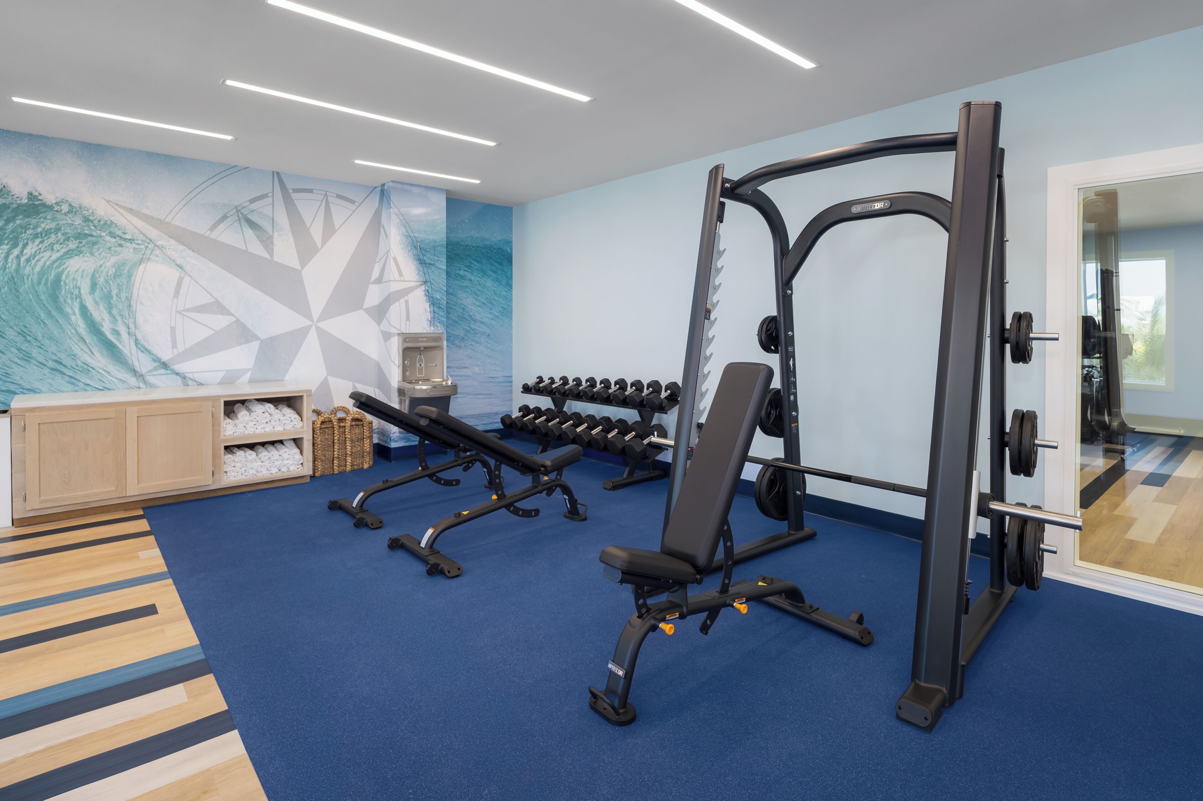 A gym with exercise equipment, a wall with geometric patterns, and a wooden cabinet with towels.