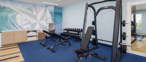 A gym with exercise equipment, a wall with geometric patterns, and a wooden cabinet with towels.