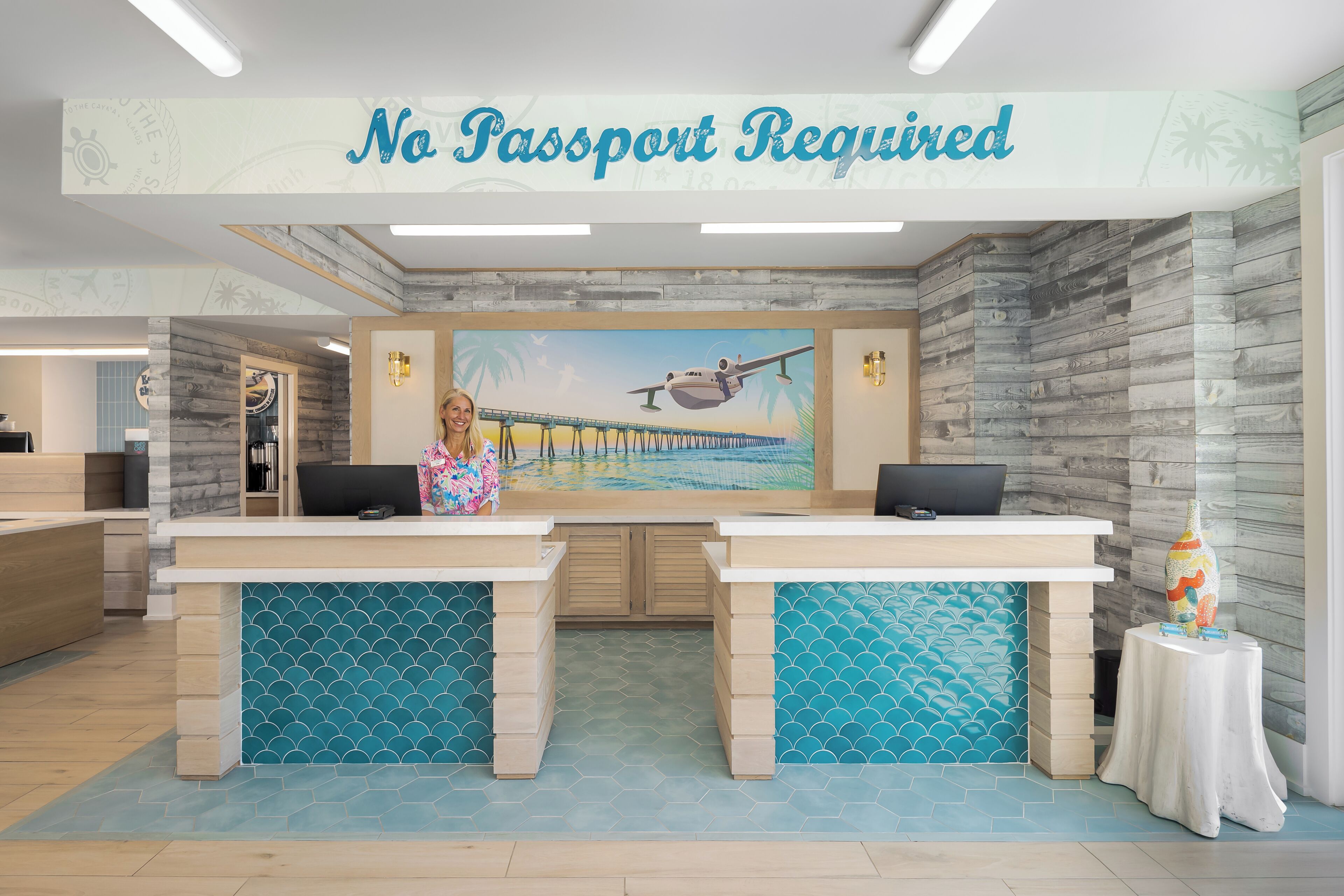 A reception desk with a 'No Passport Required' sign, a mural of a beach scene, and a wooden wall design.
