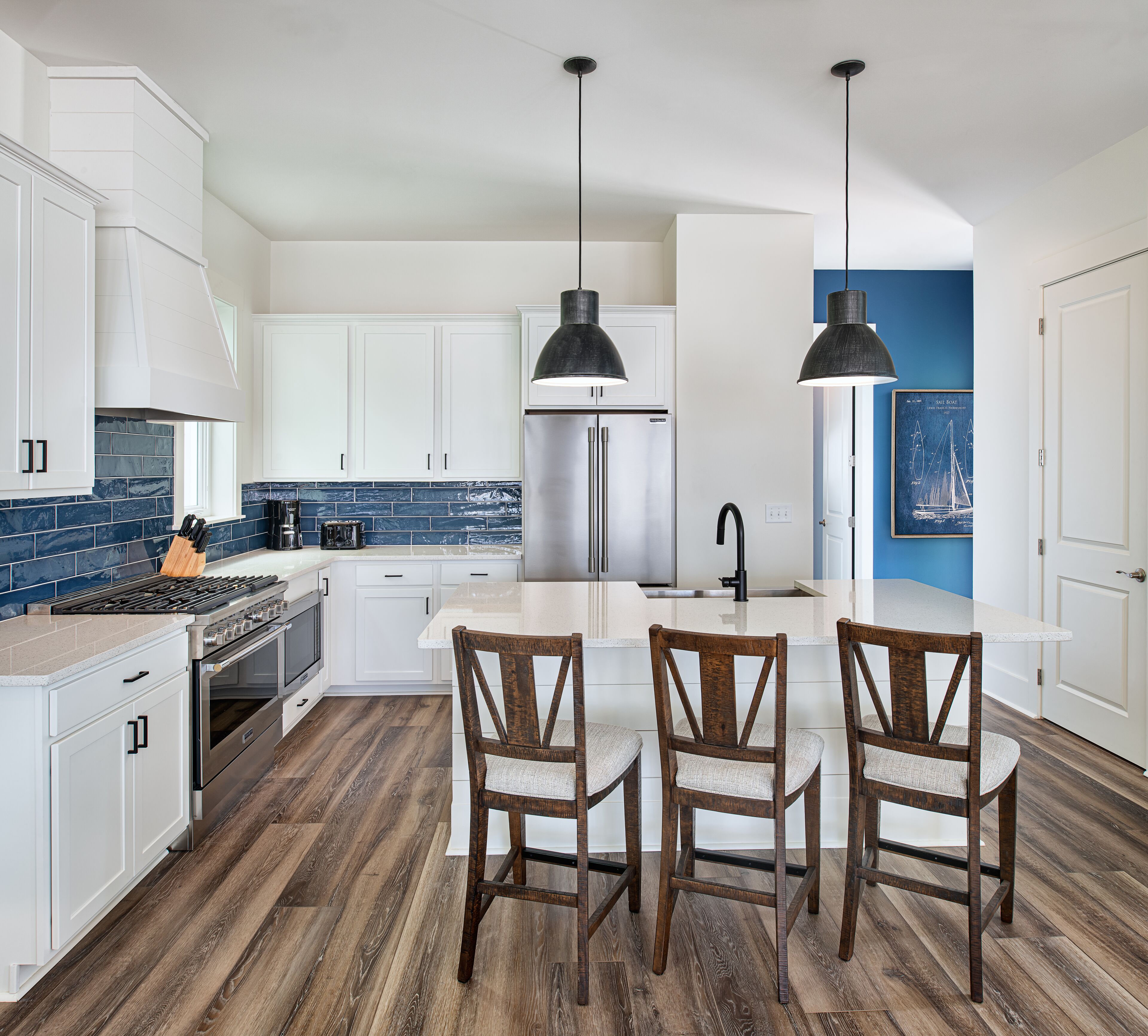 A modern kitchen with white cabinets, a stainless steel refrigerator, a wooden dining table with chairs, and a blue accent wall.