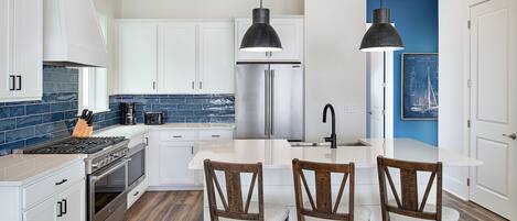 A modern kitchen with white cabinets, a stainless steel refrigerator, a wooden dining table with chairs, and a blue accent wall.