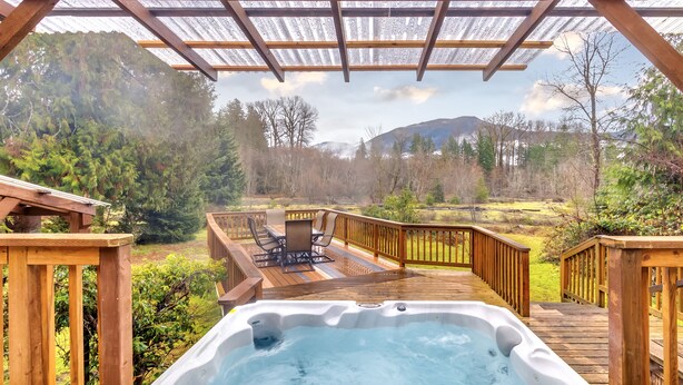A hot tub on a wooden deck with a view of a forest and mountains. - Waterfront Cabin at White Pass, Mt. Rainier (Packwood)