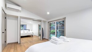 A modern bedroom with a large bed, a sliding door leading to a bathroom, and a large window with a view of greenery. - Waterfront Cabin at White Pass, Mt. Rainier (Packwood)