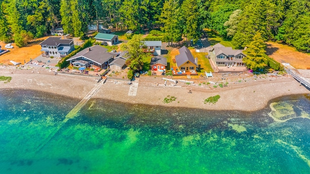 An aerial view of a coastal property with multiple houses, a beach, and clear turquoise waters.