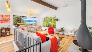 A modern living room with a large fireplace, a dining area with wooden furniture, and large windows offering a view of the outdoors.