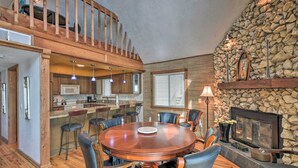 A spacious dining area with a round wooden table and leather chairs, a kitchen with wooden cabinets and a stone accent wall, and a fireplace. - Beachfront Oasis w/ Game Room, Hot Tub & Ocean Views! (Flagler Beach)