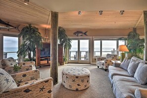 Relax in this ocean-view living room with a sofa, armchairs, and ottomans, surrounded by nautical prints and lush greenery.