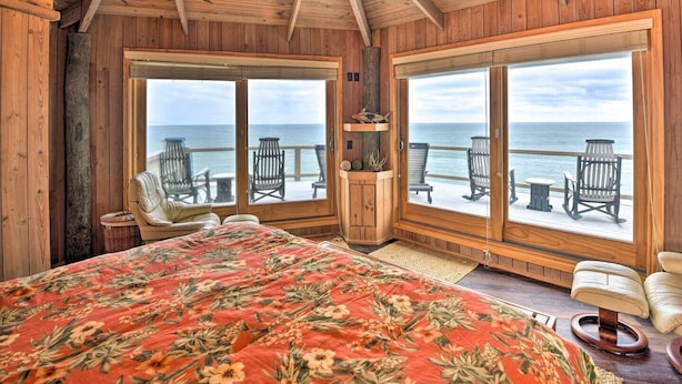 Une chambre dans une cabane en bois, avec un grand lit, deux fenêtres et une vue sur l’océan.