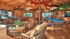 Un grand espace intérieur comprenant une table de billard, des meubles en osier et un escalier.