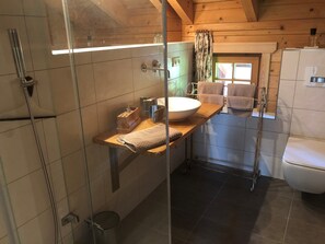 Ett badrum med en dusch som är avskärmad med glasväggar, ett handfat i trä och en toalett.