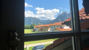 A window view of a residential area with houses, a road, and mountains in the background. - Rotes Haus Füssen Apartment Klassik (Füssen)