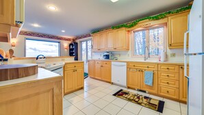 A modern kitchen with wooden cabinets, a white refrigerator, and a window with a view of trees. - 17 Mi to Skiing! Lake-View Michigan Home w/ Deck (Harbor Springs)