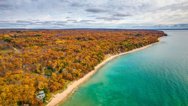 An aerial view of a coastal area with a beach, dense forest, and a clear view of the ocean. - 17 Mi to Skiing! Lake-View Michigan Home w/ Deck (Harbor Springs)