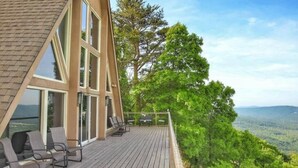 A modern house with a wooden deck, large windows, and a view of the forest.