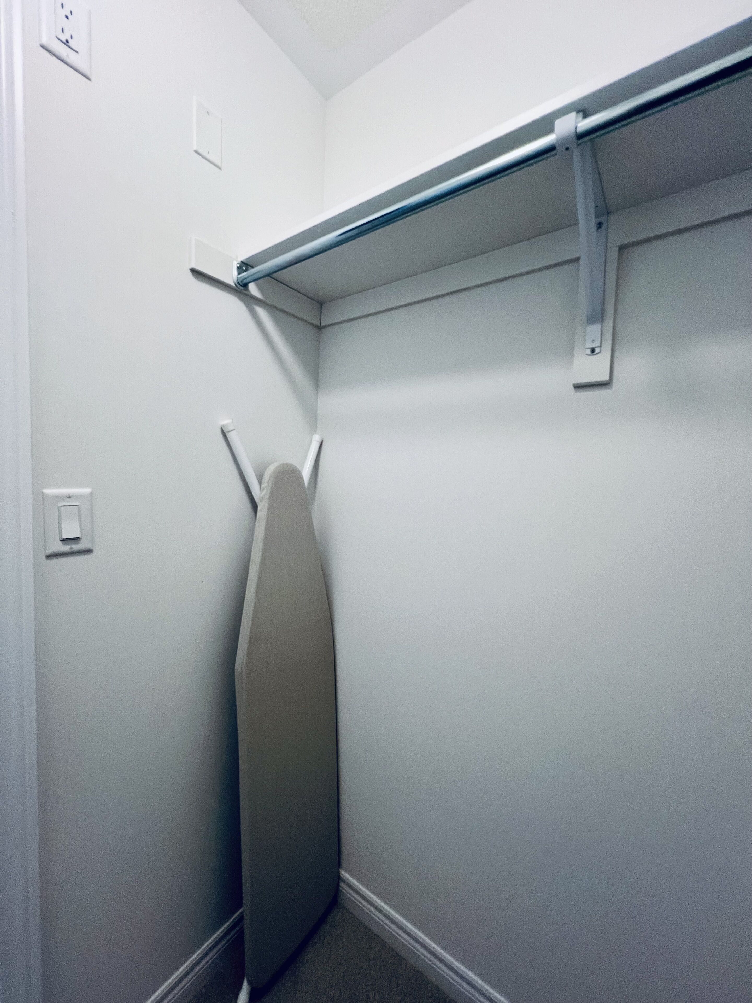 A corner of a room with a white wall, a metal shelf, and a whiteboard.