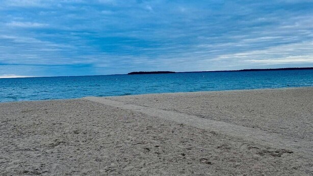 Kirkkaan taivaan ja tyynen meren reunustama ranta.