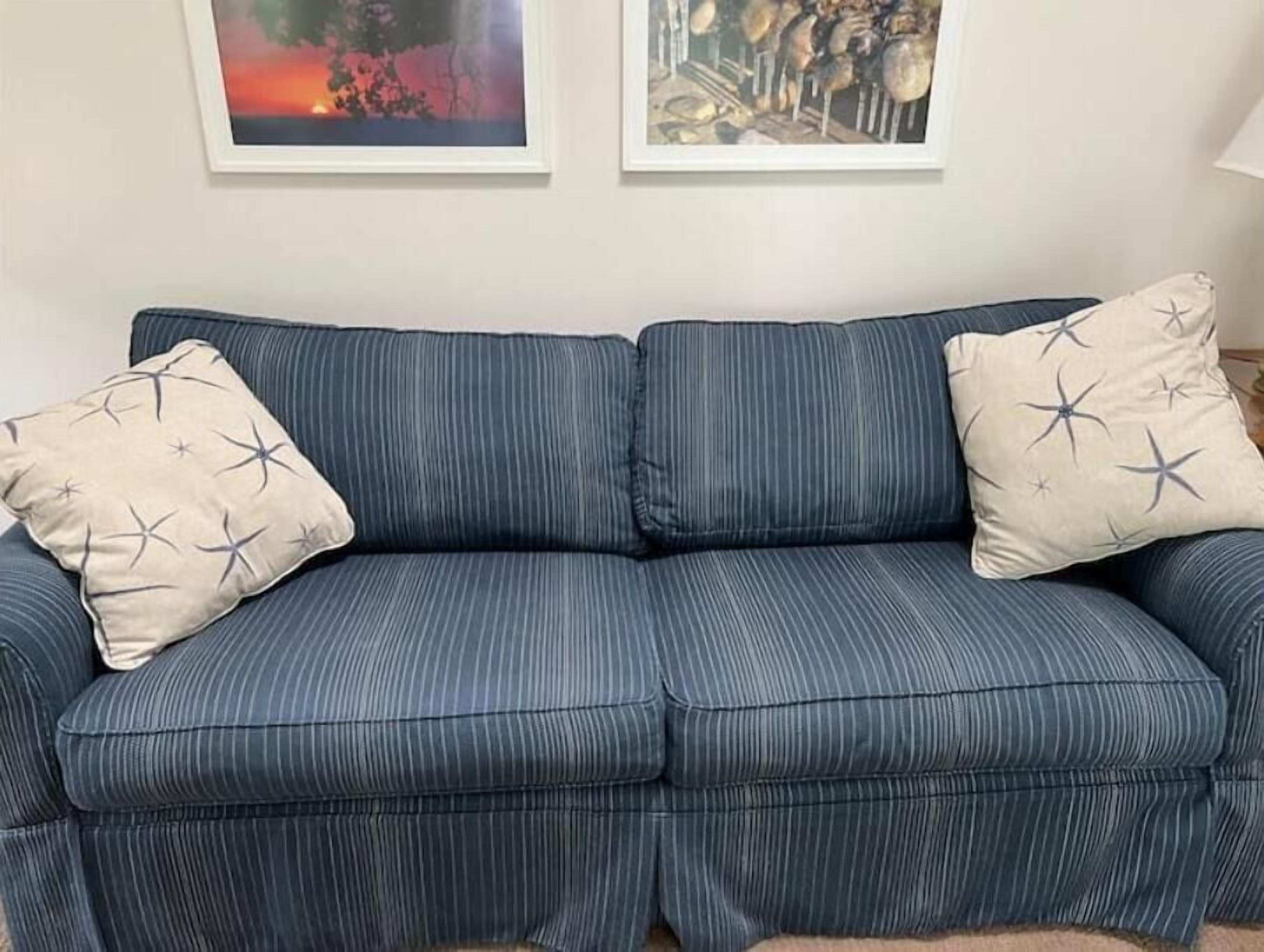 Un canapé bleu orné de coussins à motifs étoilés, deux œuvres d’art encadrées au-dessus, et un tapis de couleur claire sur le sol.