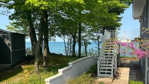 A pathway leading to a deck with a view of the sea, surrounded by greenery and a barbecue grill.