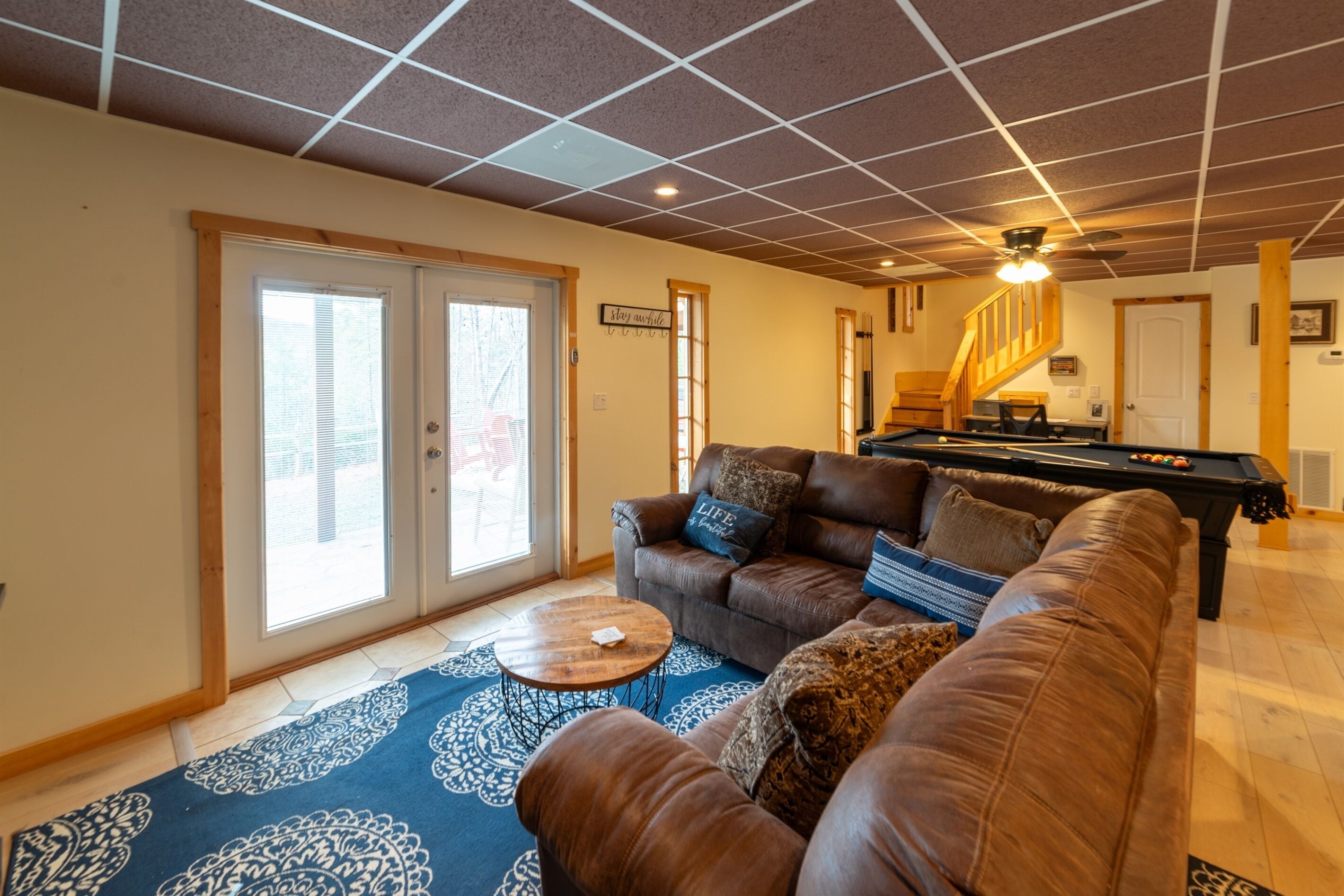 A living room with a brown leather couch, a pool table, and a blue patterned rug.