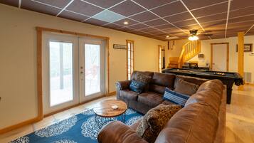A living room with a brown leather couch, a pool table, and a blue patterned rug.