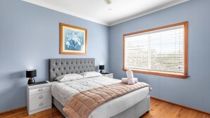 Une chambre à coucher avec un lit, des tables de chevet, une lampe, un tableau encadré et une fenêtre avec des stores.