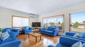 Un salon avec des canapés bleus, une table basse en bois et un téléviseur fixé au mur.
