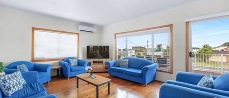 A living room with blue sofas, a wooden coffee table, and a TV on the wall.