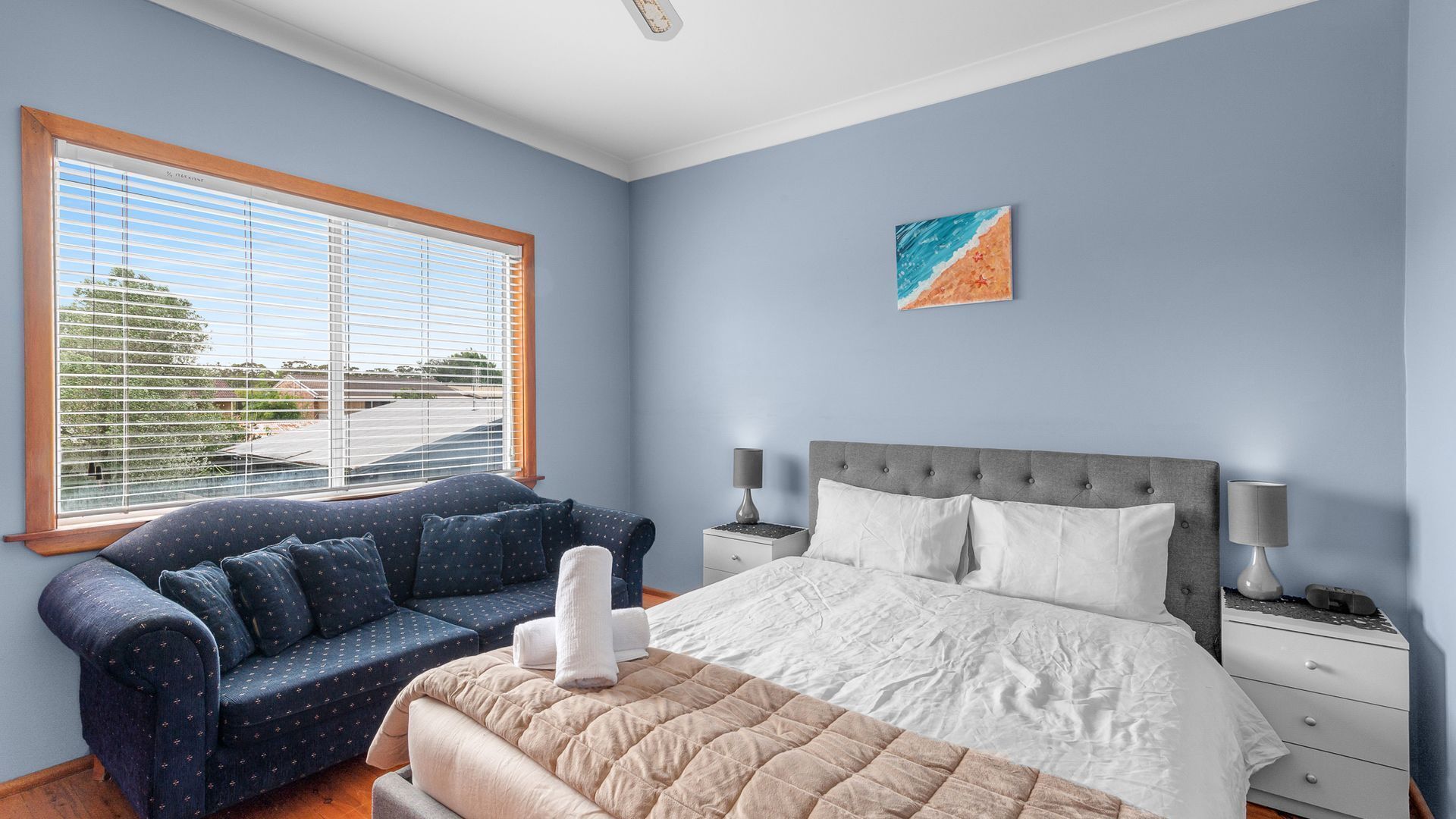 Une chambre à coucher comprenant un lit, une table de chevet, un canapé et une fenêtre avec des stores.