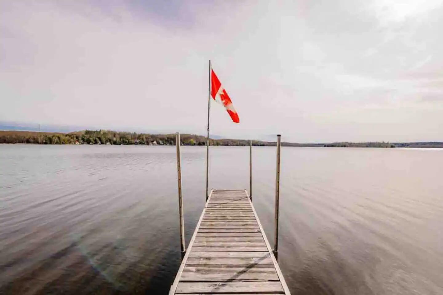 A wooden dock extending into a calm body of water with a flag on one end.