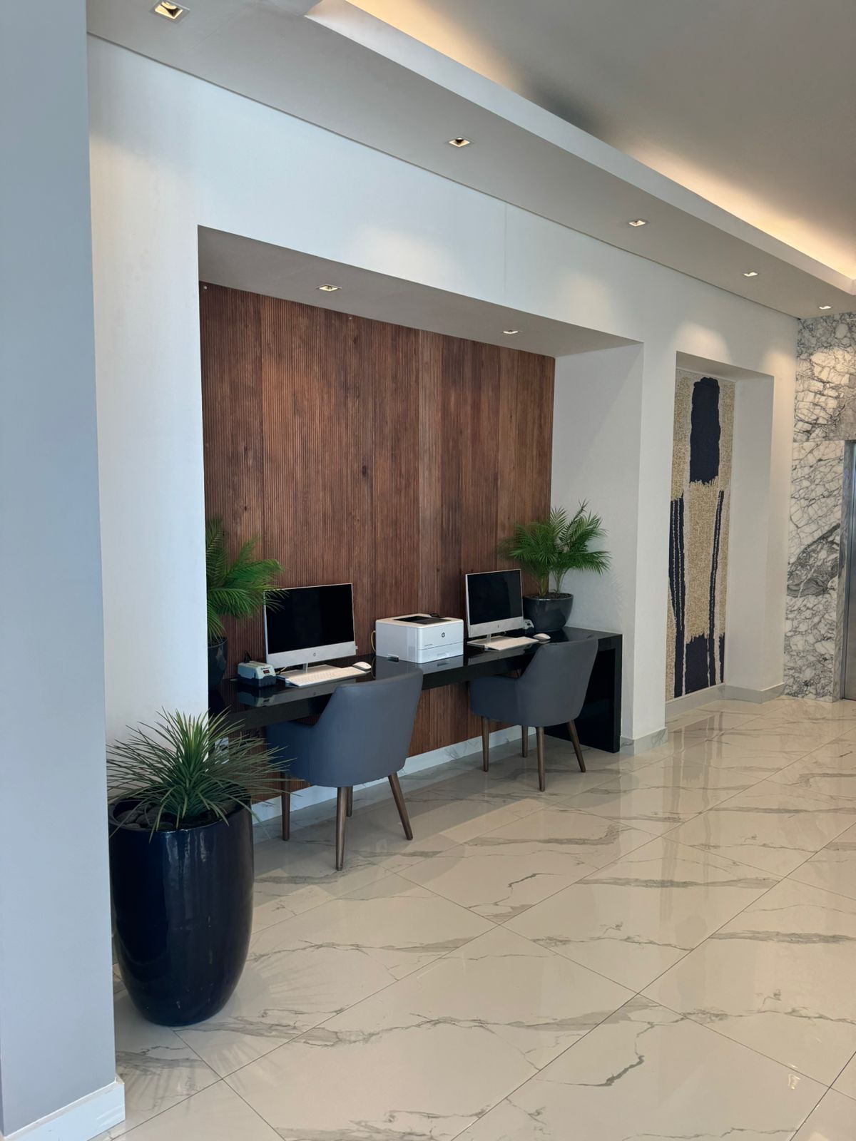 Una moderna zona de recepción con dos mostradores, cada uno con una computadora e impresora, y dos plantas en macetas.