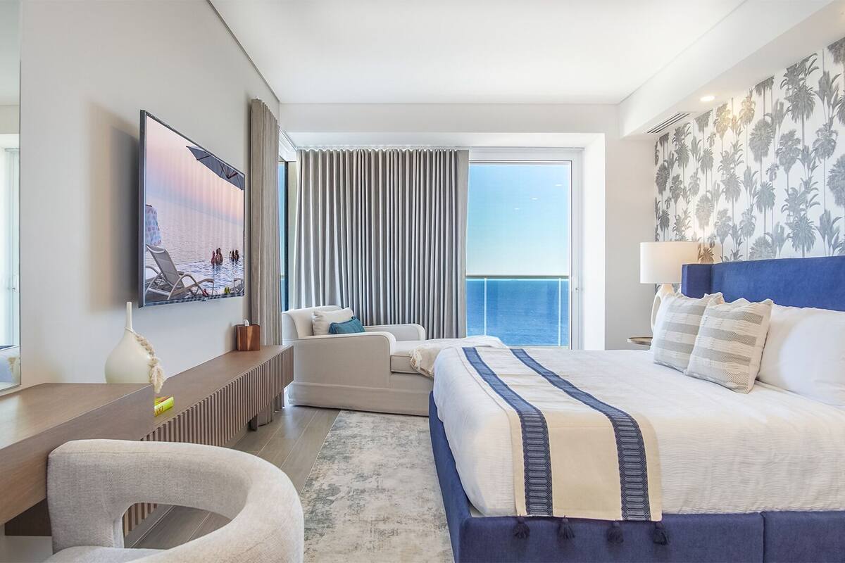 Een moderne hotelkamer met een groot bed, een bureau, een stoel en uitzicht op zee.
